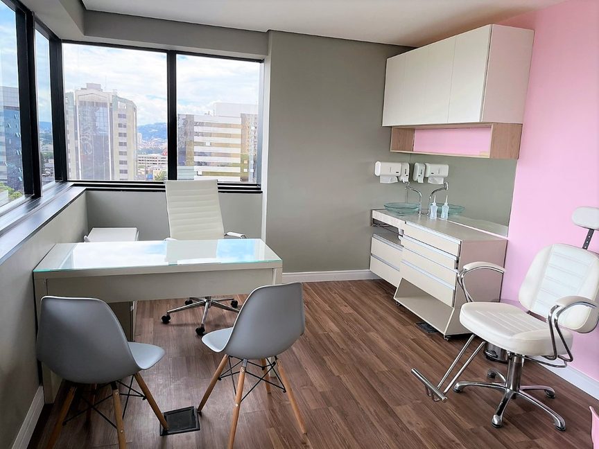 Consultório com mesa de atendimento, janelas amplas e cadeira de exame